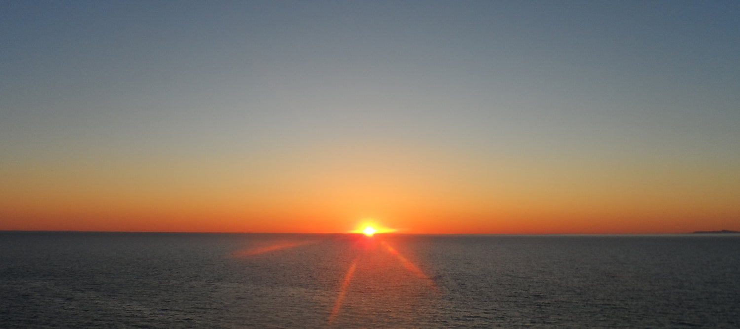 A landscape image of a sunset across a vast ocean.