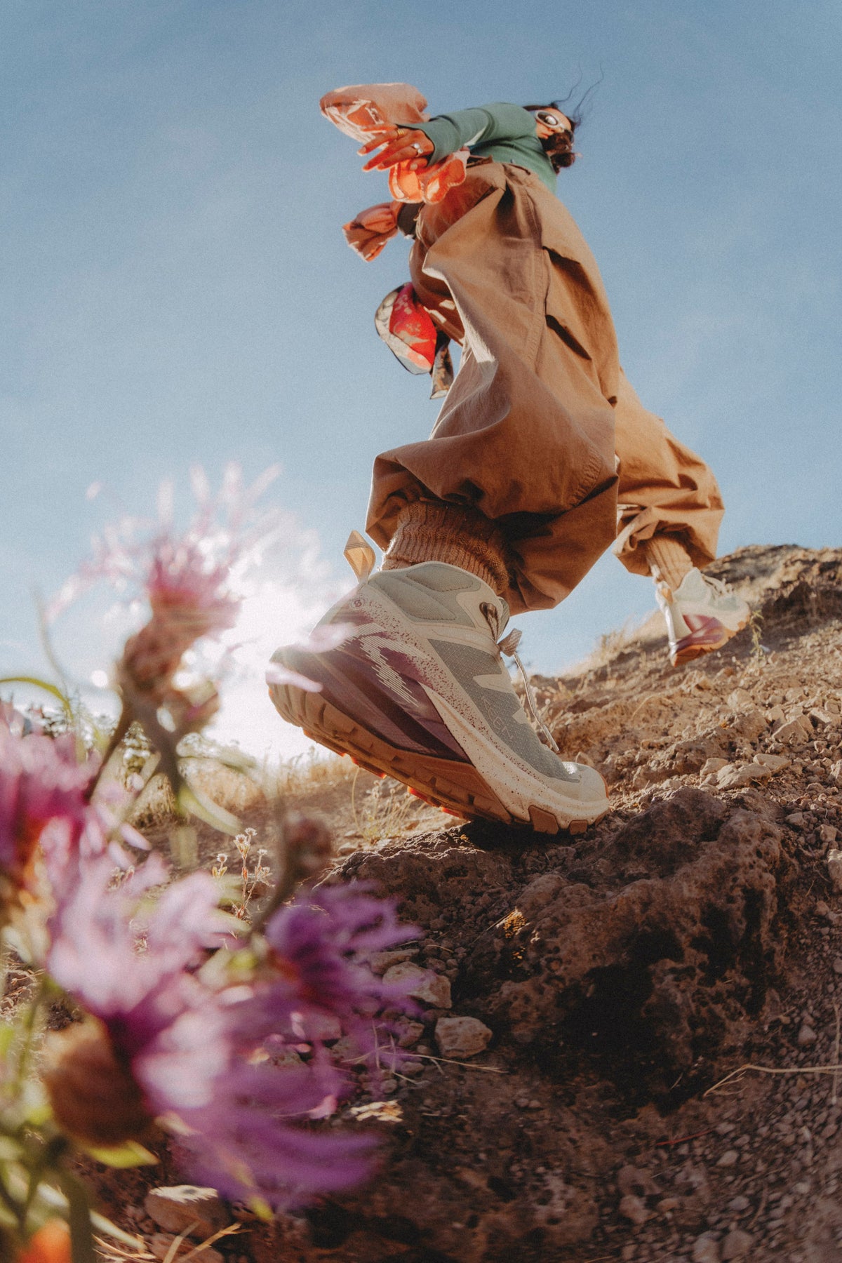 A person outdoors on rocky terrain wearing loose brown pants, a green top, and light grey targhee