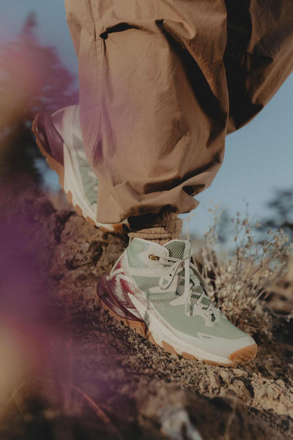 A close-up lifestyle shot of a person hiking outdoors, wearing tan pants and a light sage green