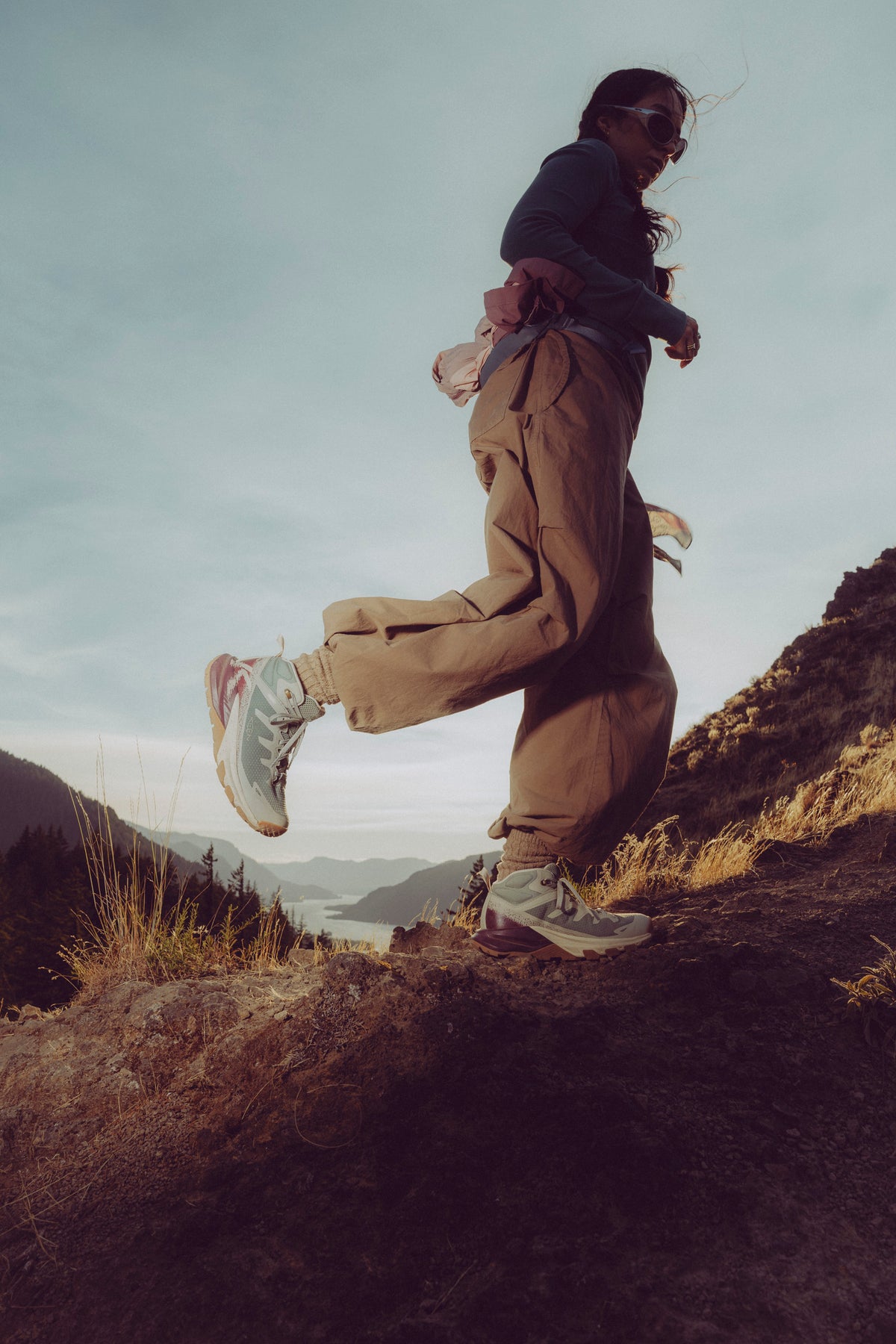 A person running outdoors on a rocky mountain slope, wearing loose brown pants, a dark long-sleeve
