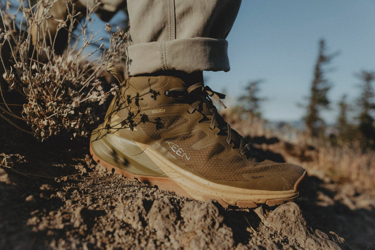 A close-up outdoor shot of a person wearing a brown keen targhee apex hiking boot on rocky ground