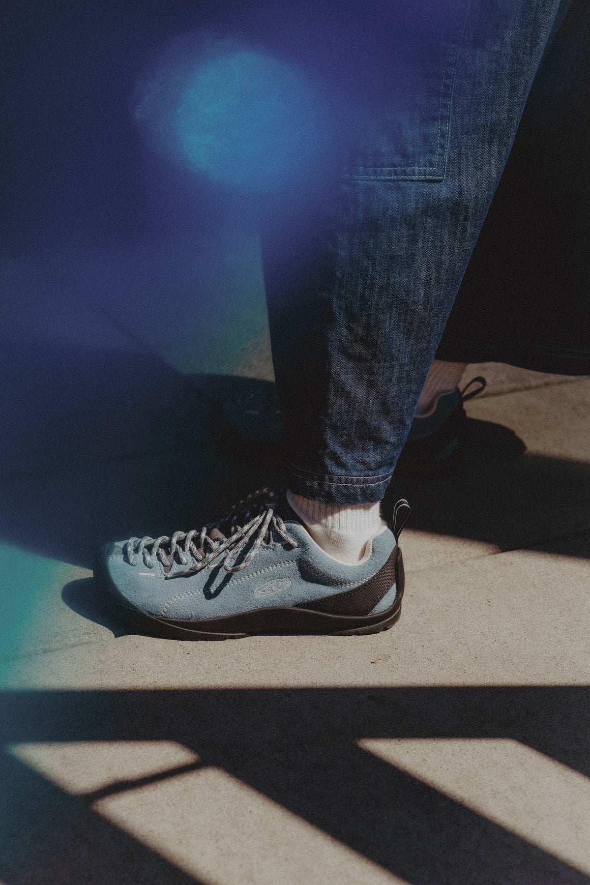 A person wearing a light blue leen jasper suede sneaker with dark brown accents, paired with dark