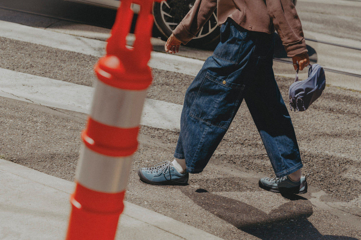 A person walking across a street crosswalk wearing baggy dark blue denim jeans, a brown top