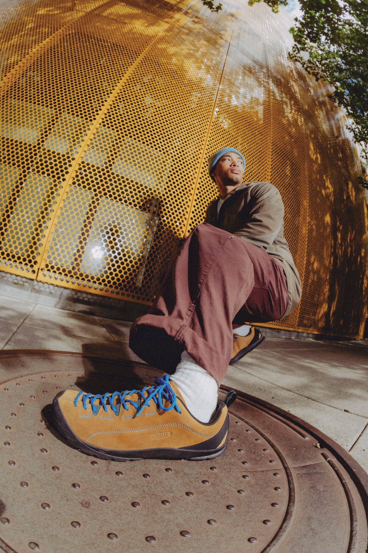 A person sitting outdoors in front of a large golden perforated metal dome, wearing a keen tan