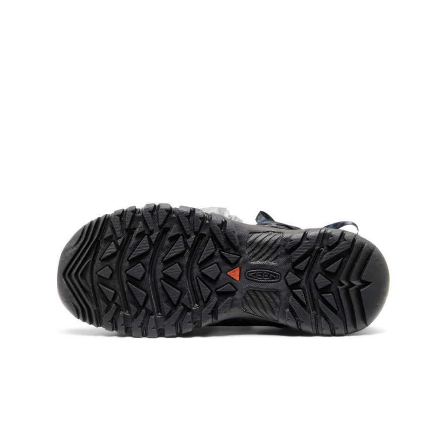 A close-up, bottom view of a black outdoor boot's rugged treaded sole