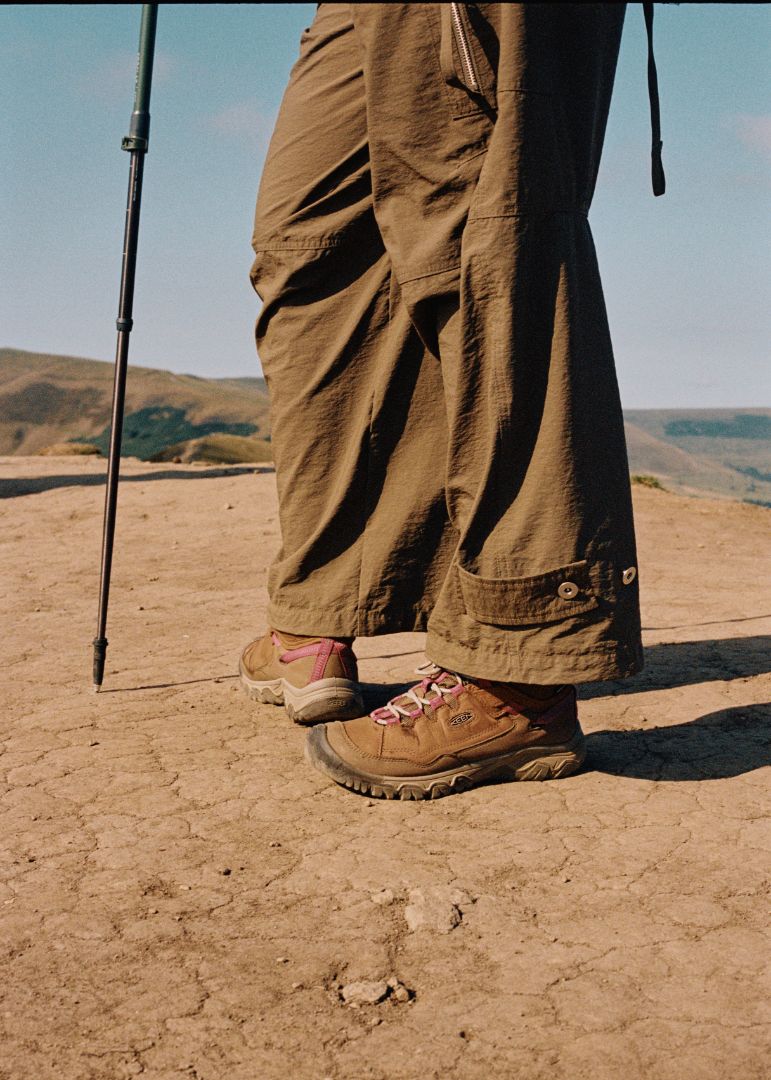 Person wearing brown pants and Targhee IV boots standing on a dirt path with a landscape in the background