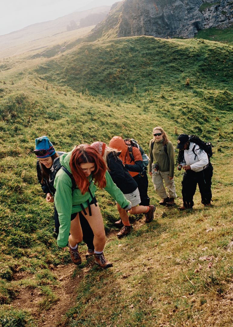 Group of people hiking on a grassy hillside with mountains in the background
