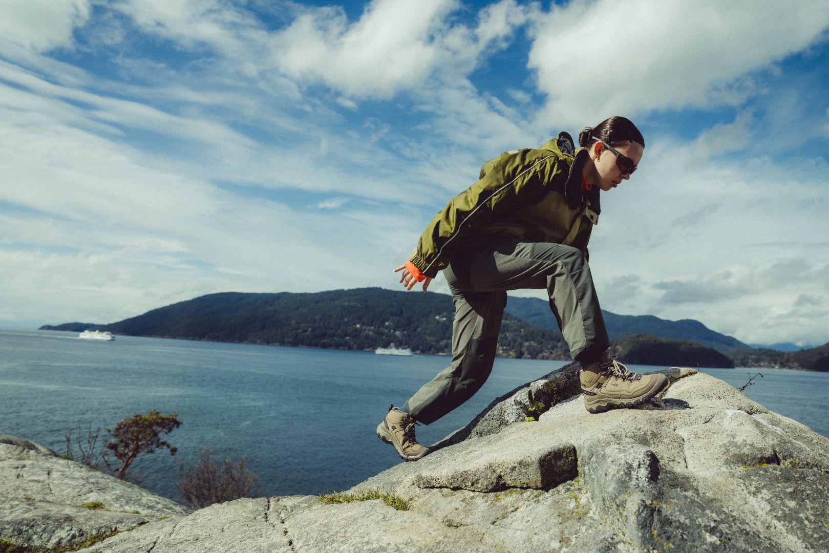 Person hiking on a rocky outcrop with a scenic view of water and mountains.