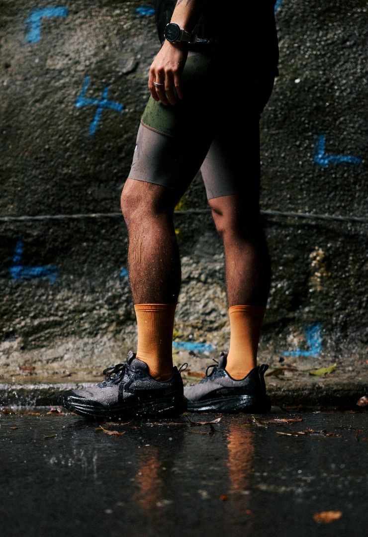 A person standing outdoors in the rain wearing dark athletic shorts and keen trail running shoes