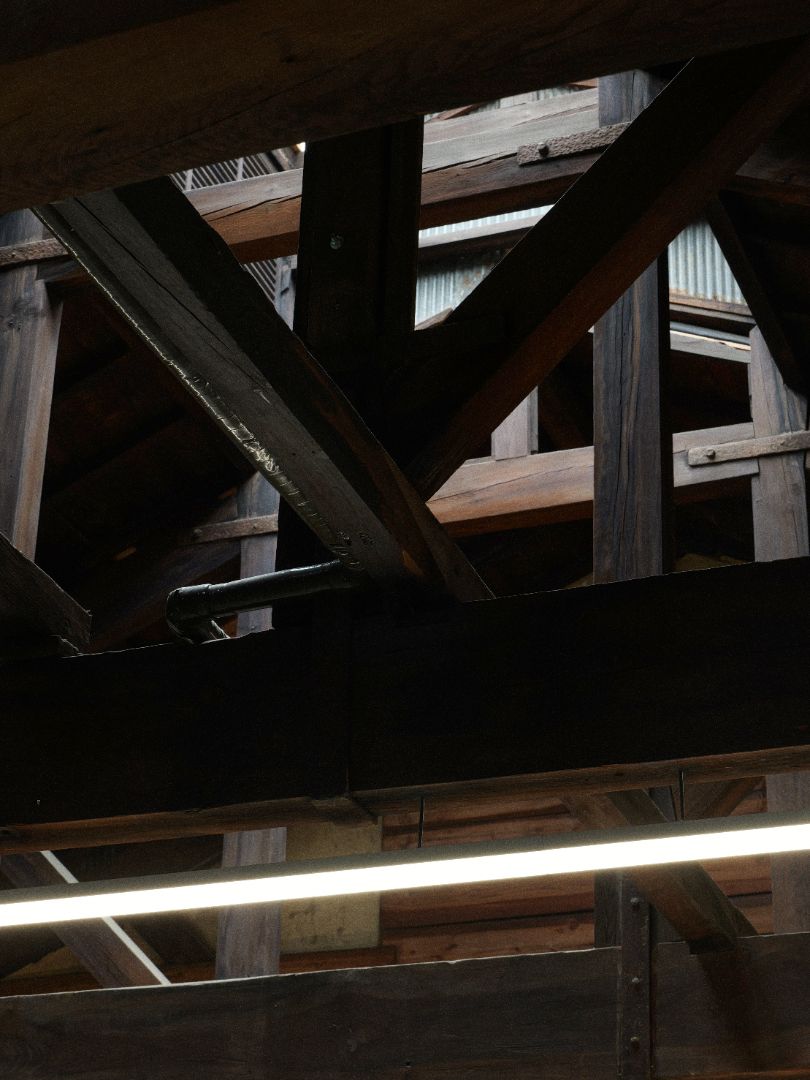 An upward-looking view inside a rustic wooden structure, showing dark stained beams, support posts