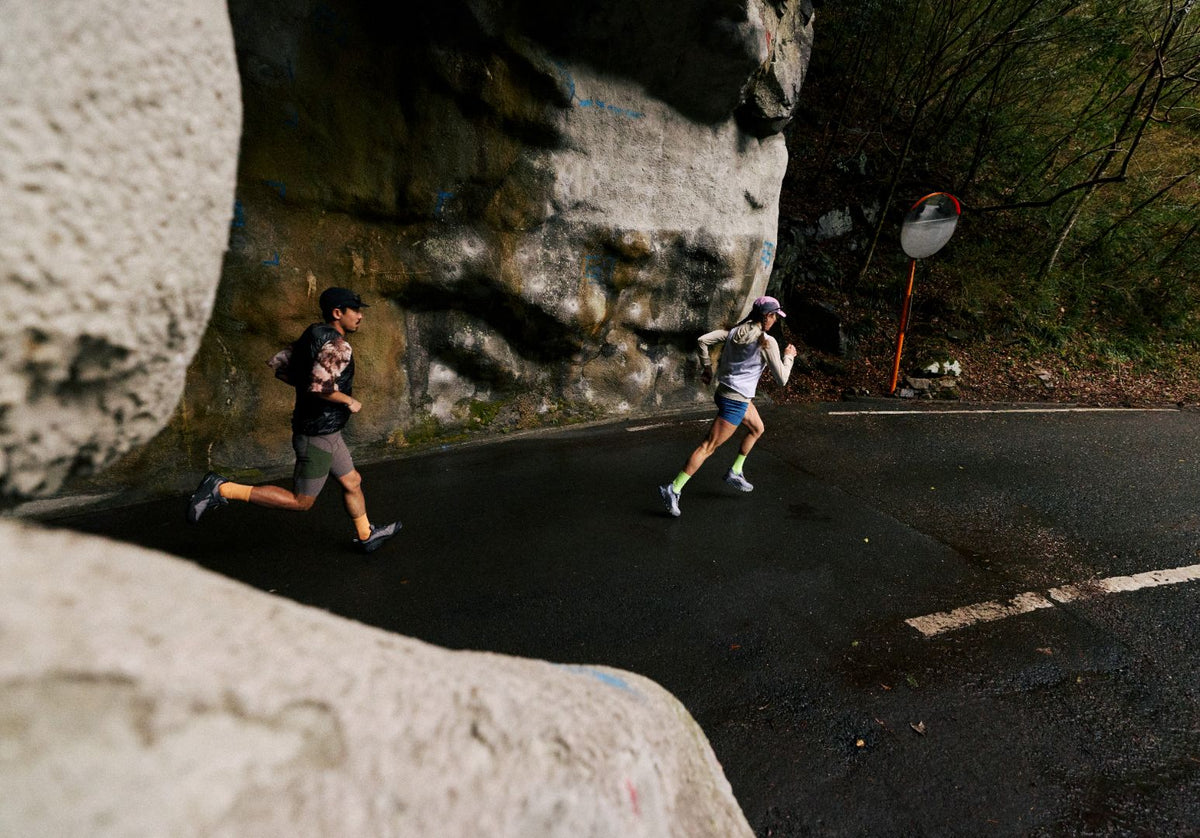 Two trail runners running along a paved road between large rock cliffs.