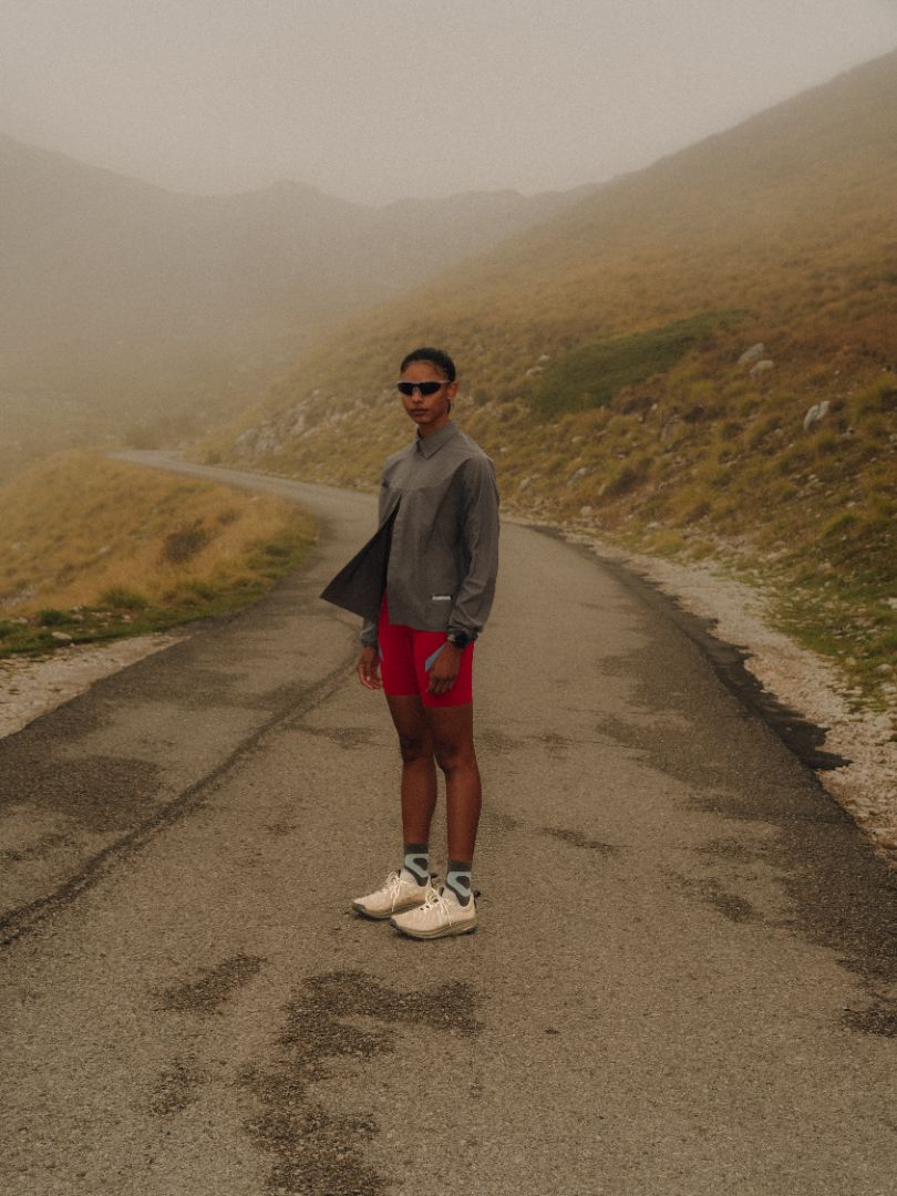 Person standing on a foggy mountain road wearing sunglasses and athletic clothing.
