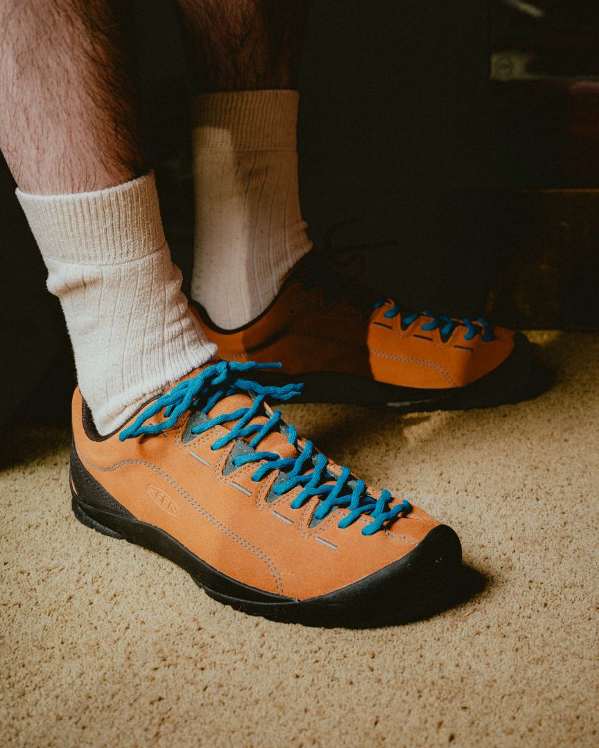 Person wearing keen jaspers in brown with blue laces on a carpeted floor