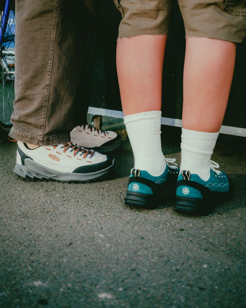 Two pairs of shoes on a concrete surface, one pair in white and black, the other in teal and black.