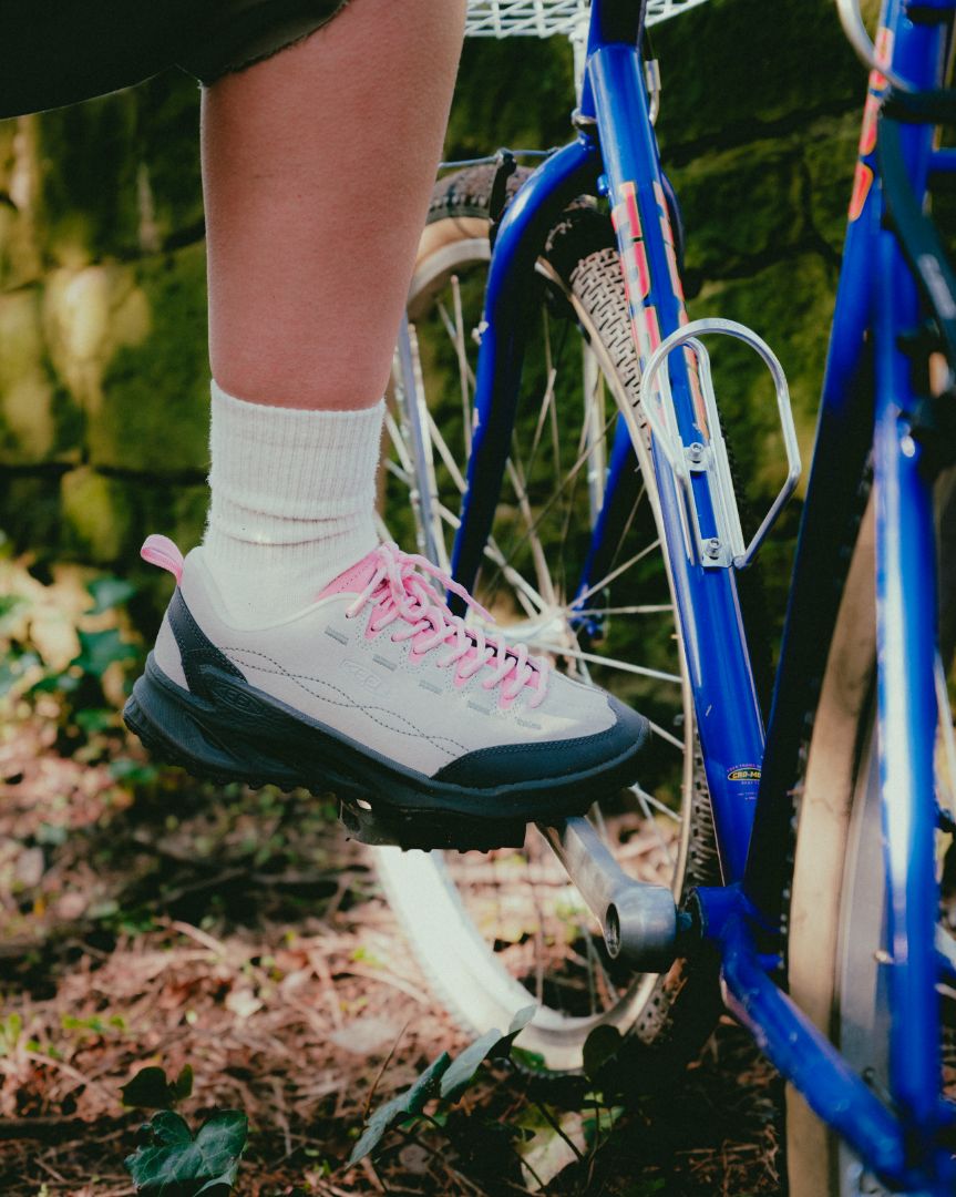 Person wearing a grey Keen Jasper Zionic Sneaker and with pink laces with a blue bicycle in the background