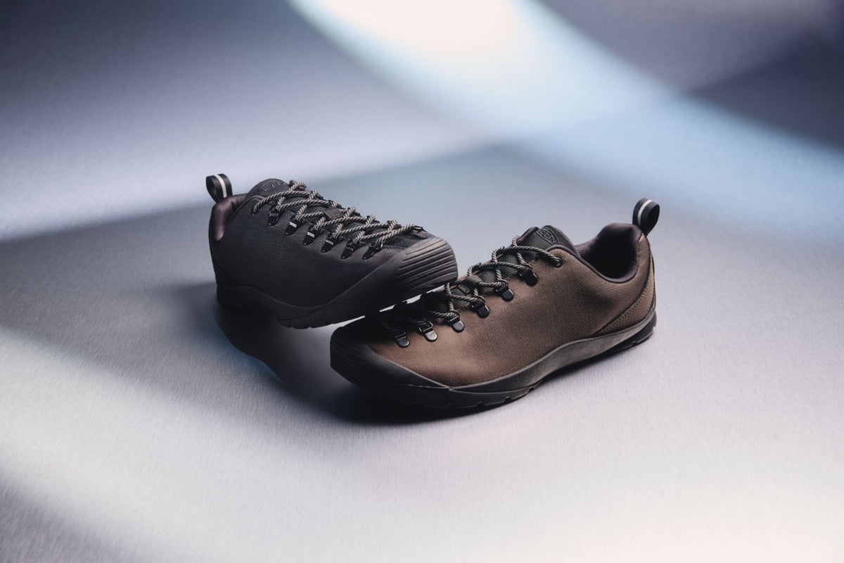 A pair of dark brown nylon trainers, positioned on a dark grey surface 