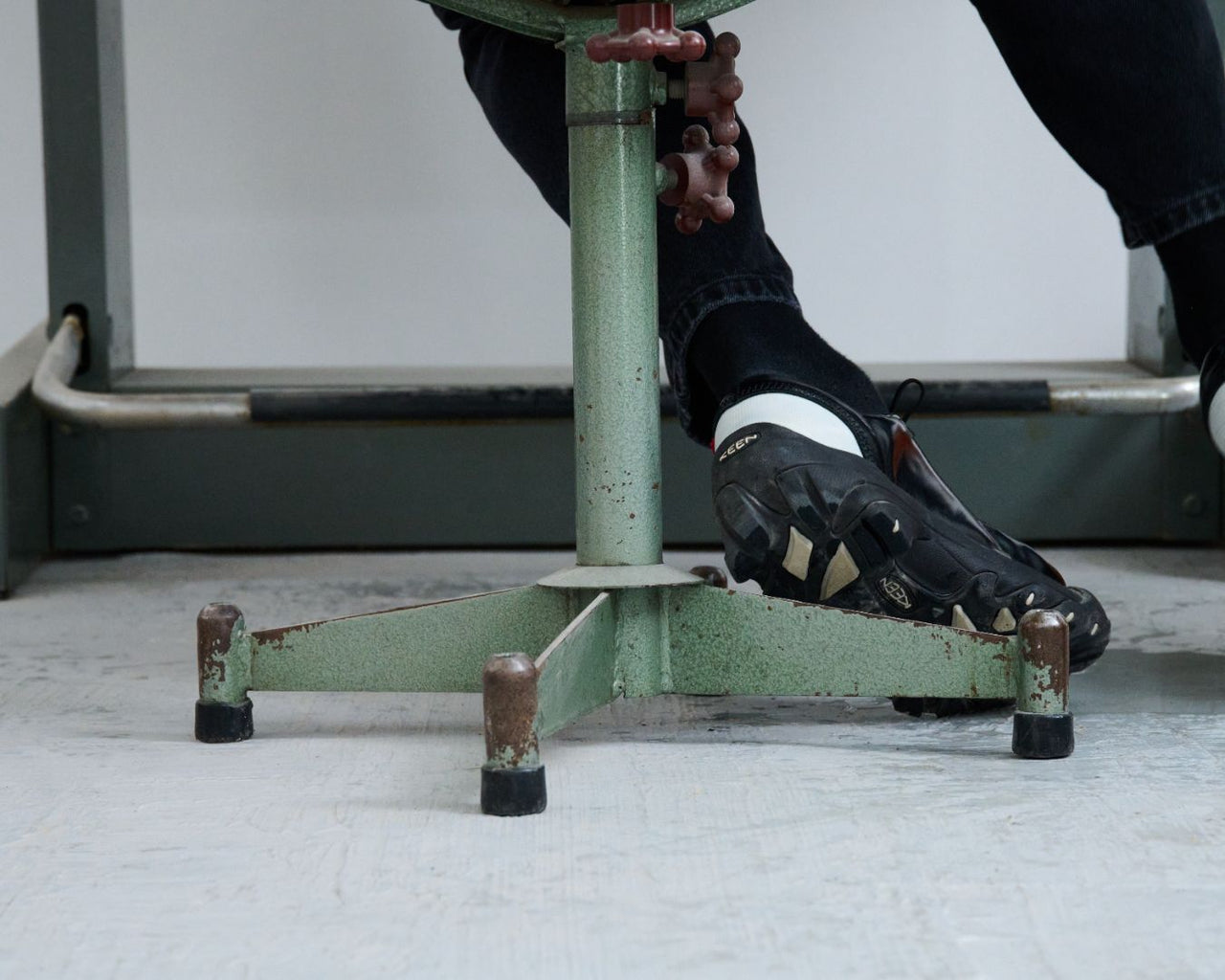 Man sitting on green metal chair in a workshop setting. He is wearing the Targher Keen X Phileo collab shoe
