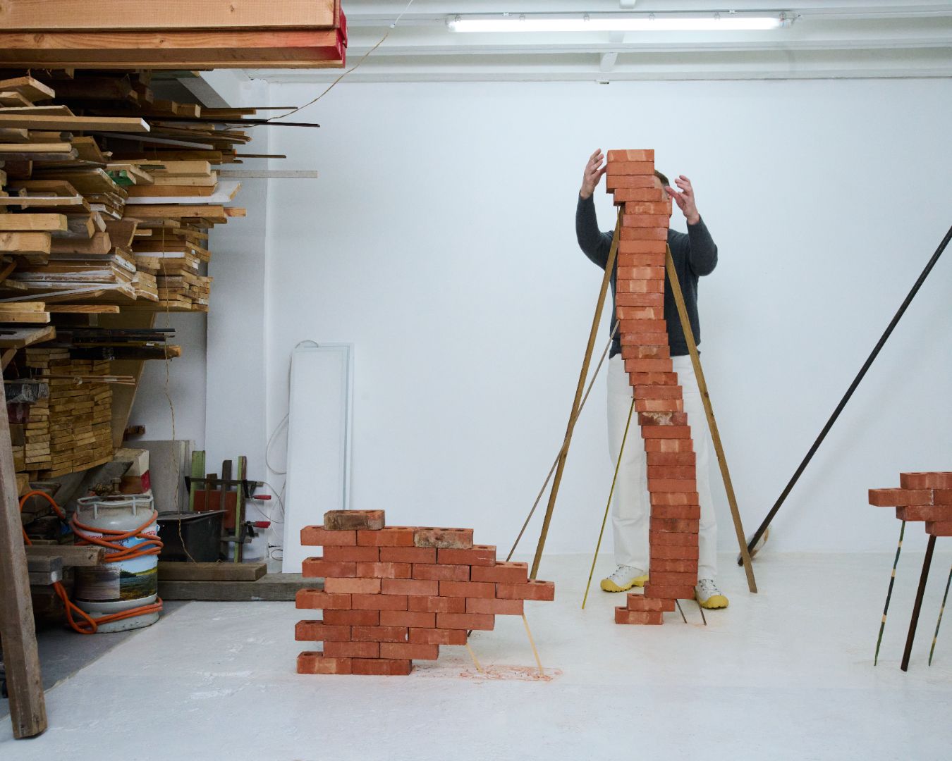 Person constructing a large tower of red bricks in a workshop setting. Wearing the Phileo X Keen collab shoes in White.