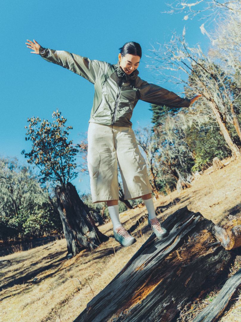 women looking happy balancing on a log in a natural setting with trees and clear sky. She is wearing the Jasper sneakers in a pale green colour