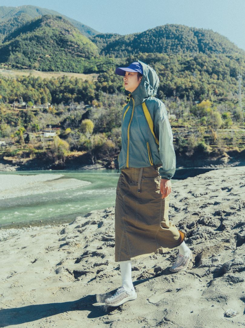 KEEN UNEEK footwear with braided cord uppers and cushioned soles worn while walking on sandy river terrain, showing flexible construction and outdoor‑ready grip