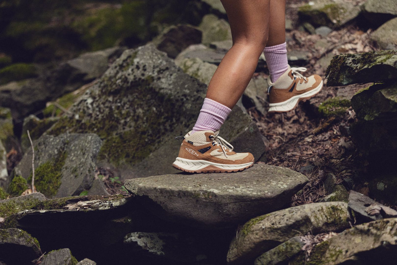 Person wearing Hightrail hiking shoes in a light brown colour paired with pink socks walking up a rocky path