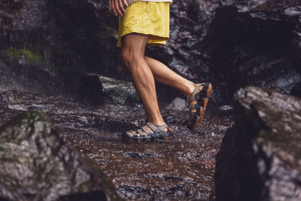 Person walking on a wet rocky surface wearing Keen Hyperport sandals and Yellow Shorts.
