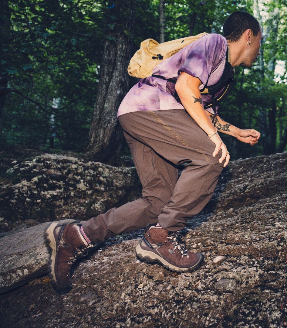Person hiking in a forest, sitting on a log with a backpack.