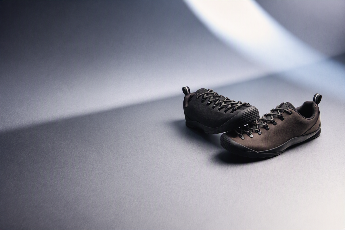 A pair of dark brown nylon trainers, positioned on a dark grey surface 