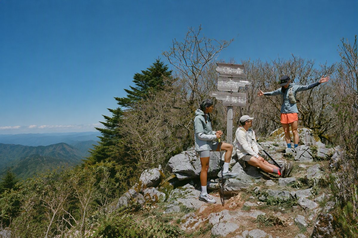 Three hikers pause on a rocky mountain summit with a trail signpost.