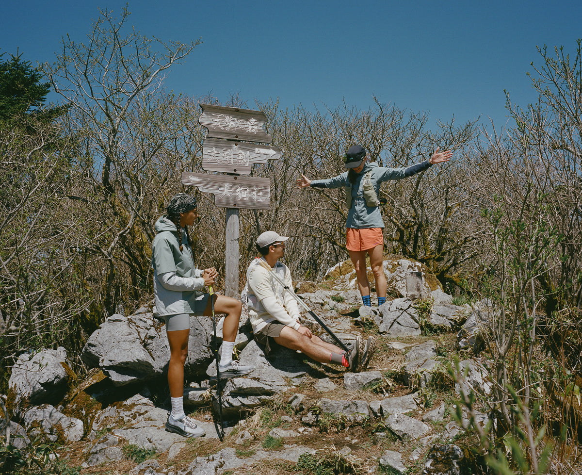Three people hiking on a rocky mountain summit with a wooden signpost, 