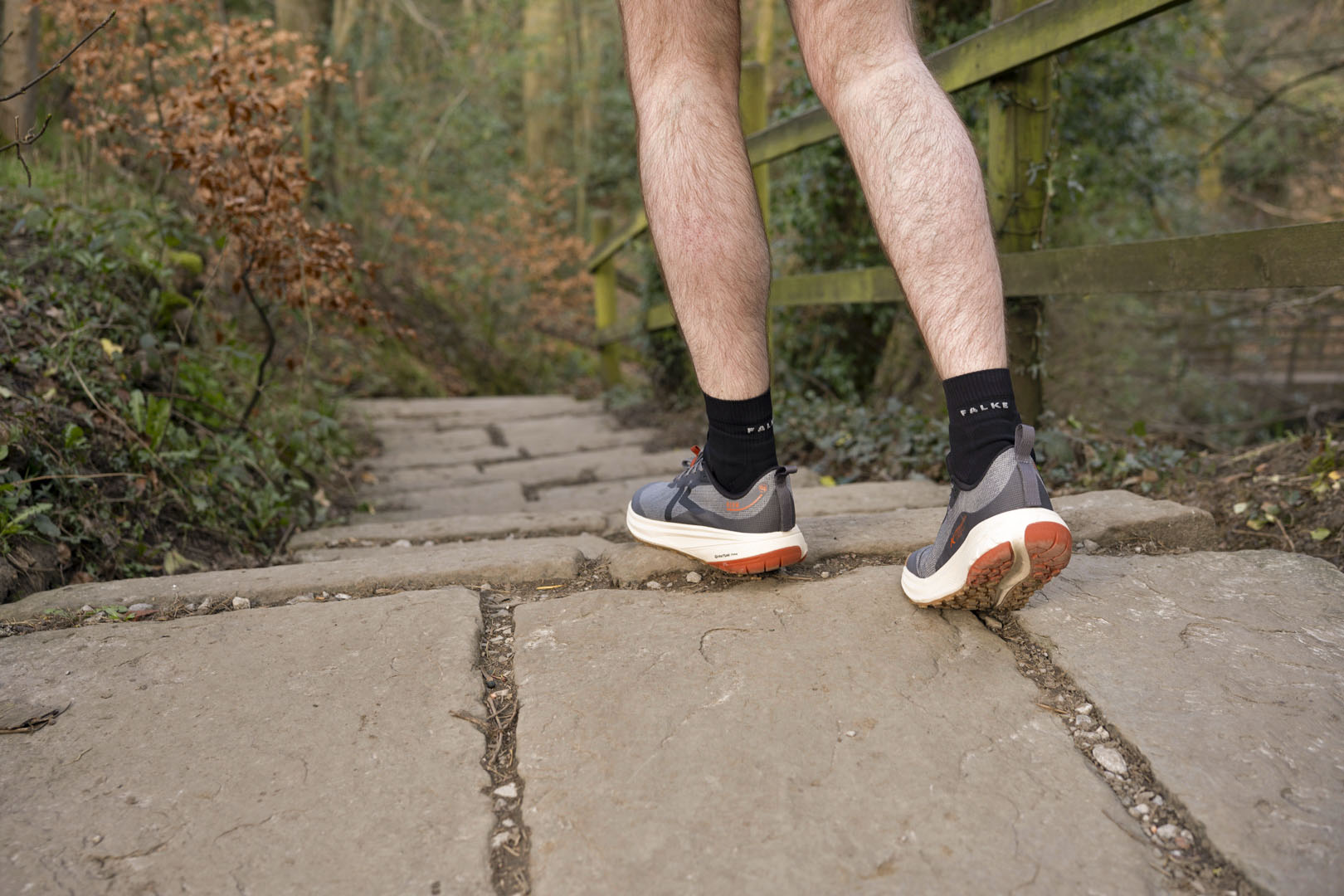 Person walking outdoors on a stone path with black socks and Keen Roam Trail Running shoes.