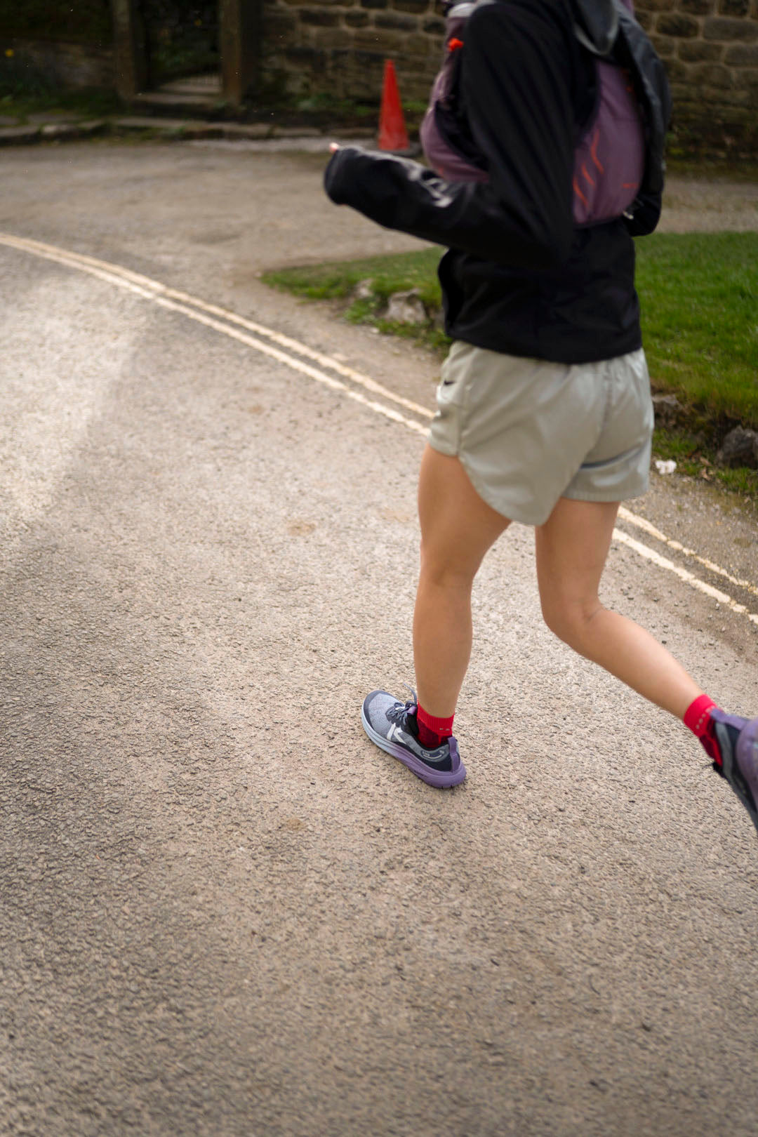 Person running on a road wearing Keen Roam Trail running shoes with a stone wall and cone in the background