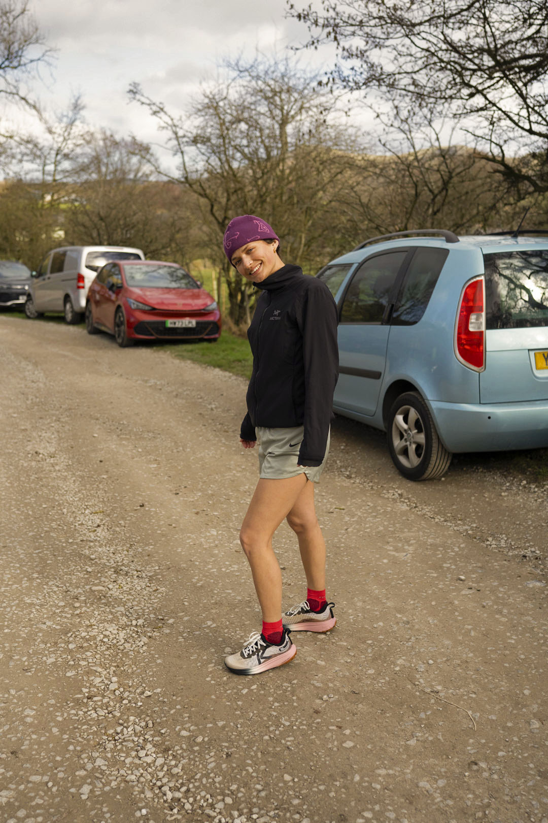 Person standing on a dirt road with parked cars in the background