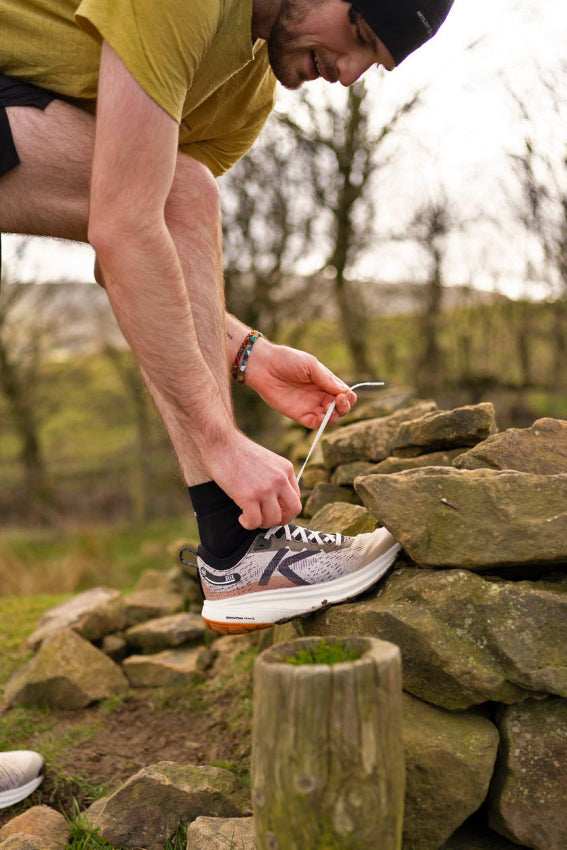A runner is tying their shoelace whilst resting their shoe on a rock pile. 