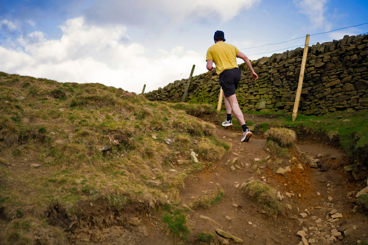 Person wearing a yellow t-shirt running on a grassy hill with a stone wall and blue sky in the background