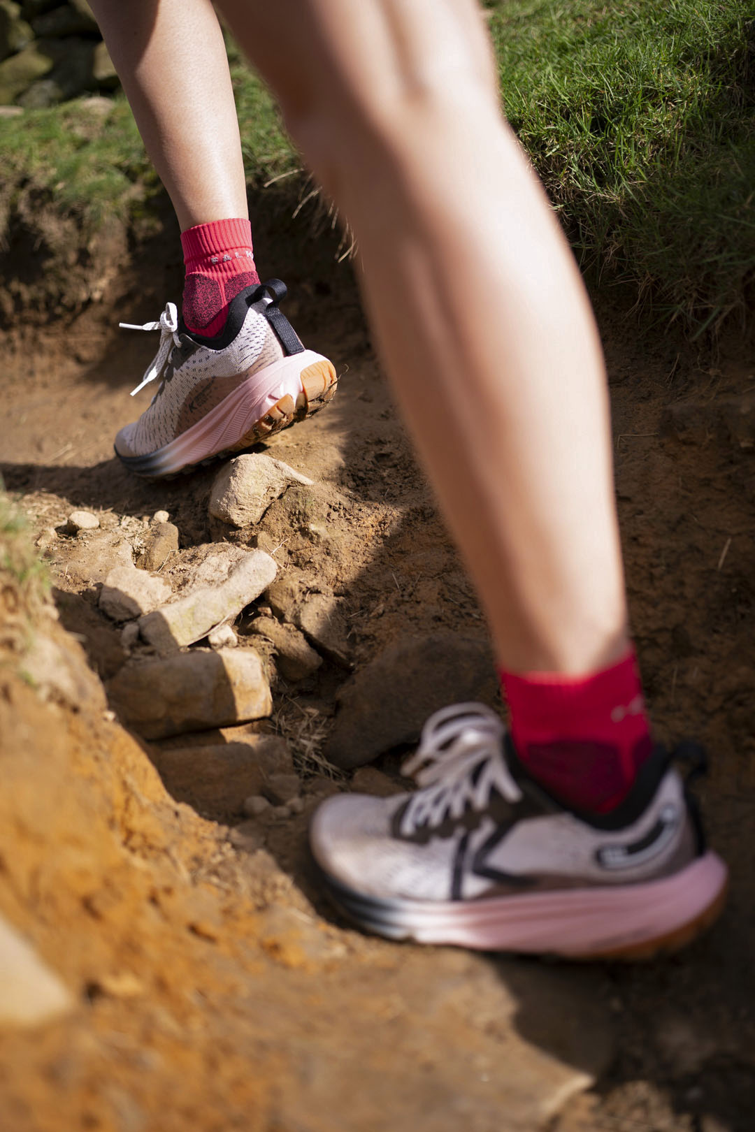 Person running on a rocky trail wearing keen trail running  shoes and pink socks.