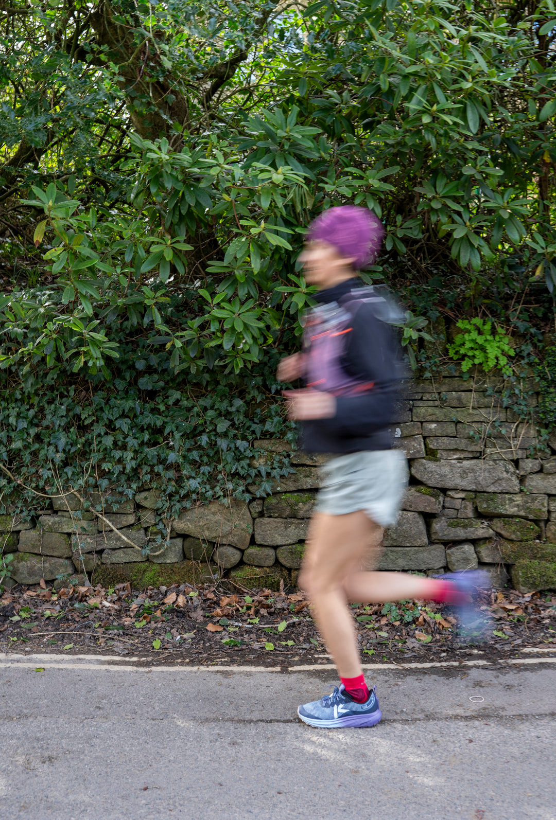 Person running on a road with greenery and a stone wall in the background