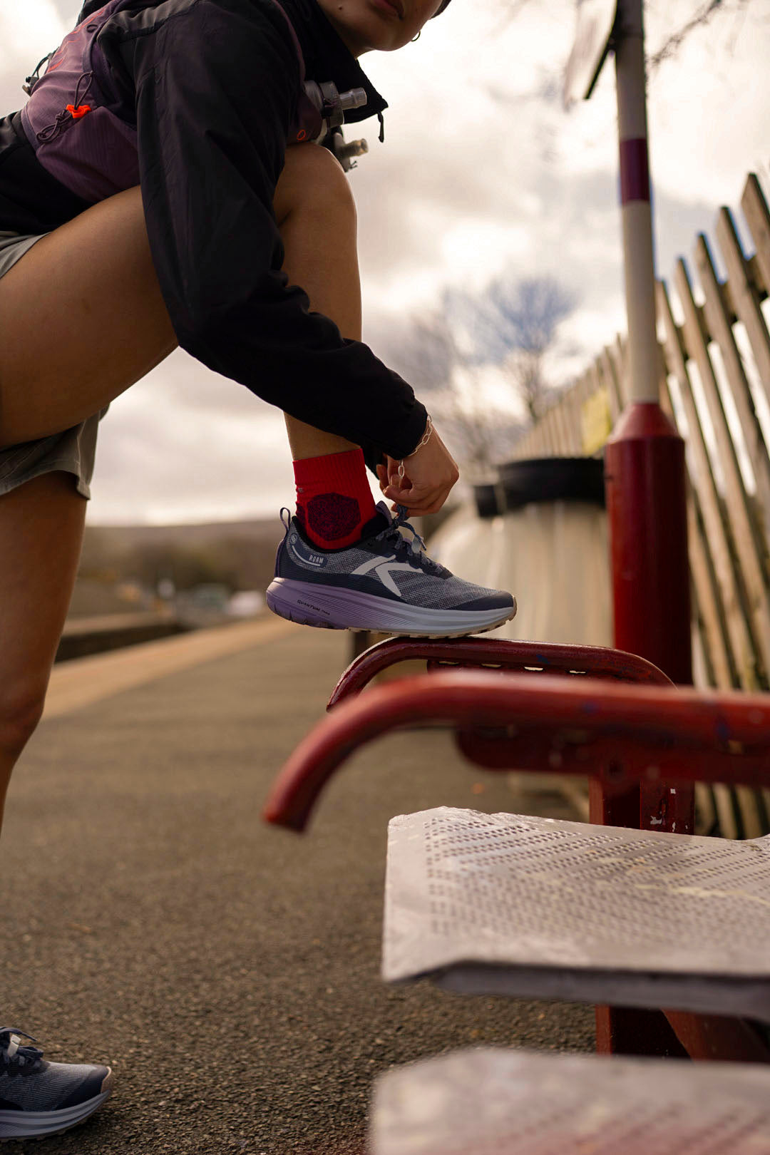 Person wearing Keen Roam trail running  shoes adjusting their lace on a bench with a cityscape background