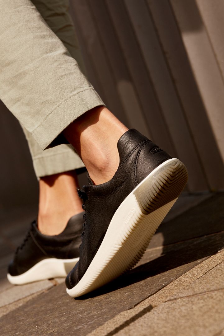 Keen black KNX sneakers with white soles worn by a person on a textured surface