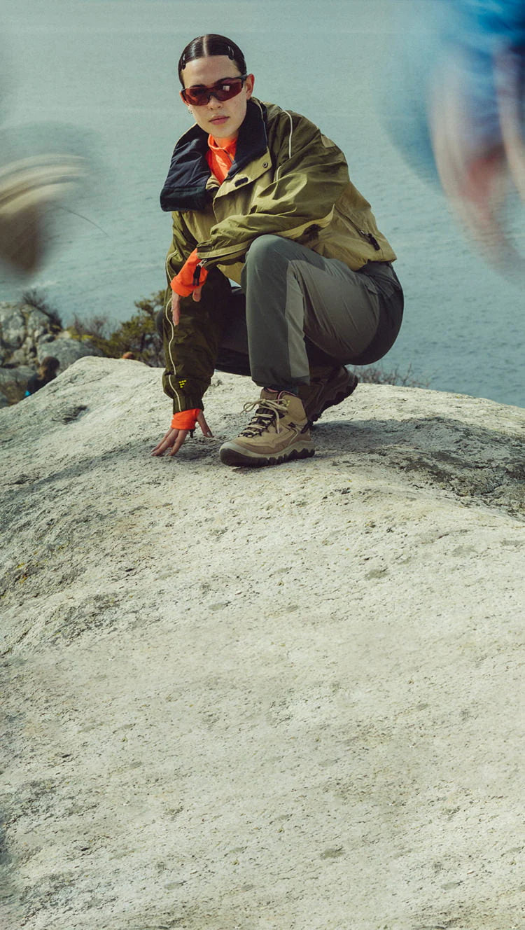 Person in outdoor setting wearing sunglasses and green jacket on rocky terrain