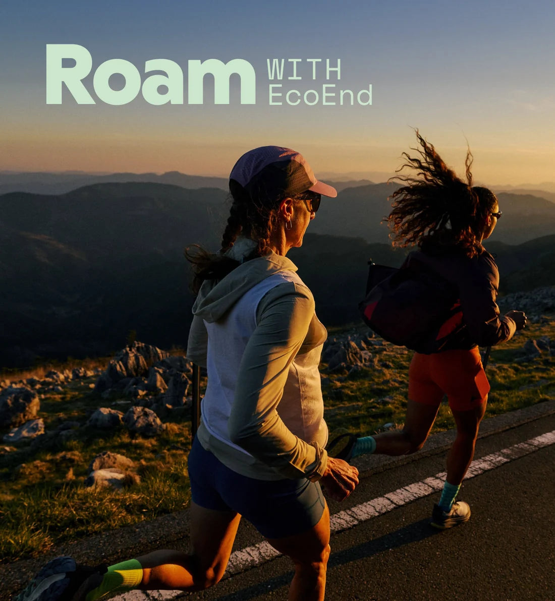 Two female runners jogging on a mountain road during golden hour, with the text 'Roam WITH EcoEnd' on top.