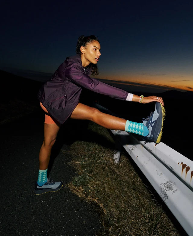 Woman stretching on a road at night with a dark sky and horizon.