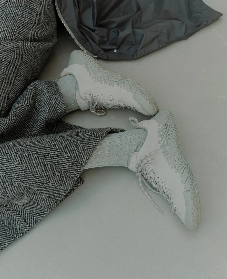 A pair of white low-top sneakers with textured soles, worn with light gray socks and paired