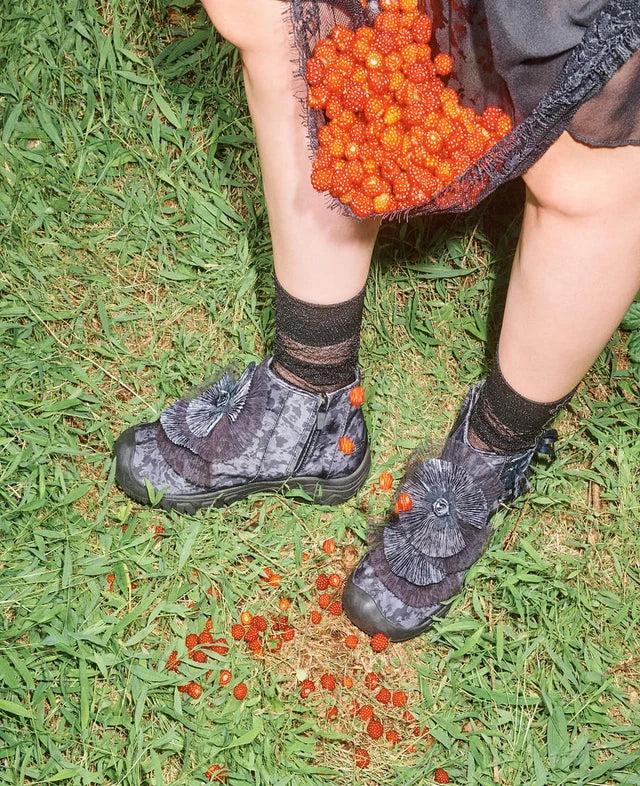 A person sitting on grass outdoors wearing dark patterned boots with decorative flower embellishments