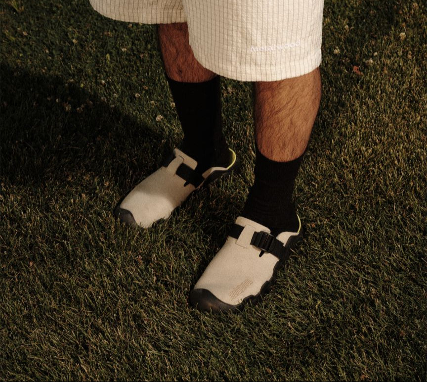 Person wearing checkered shorts and white sandals with black soles on grass