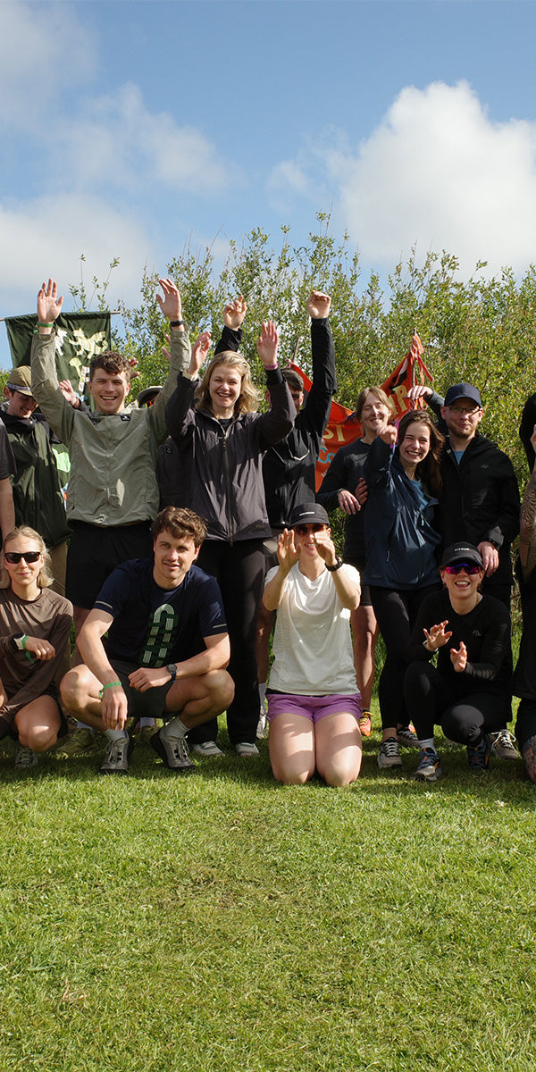 Group of people posing outdoors with raised hands on a grassy field.
