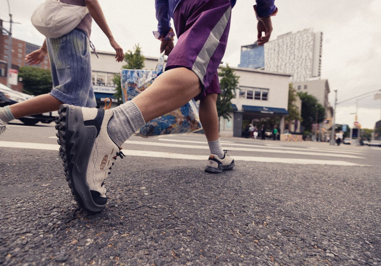 Two people walking on a street with one person wearing purple shorts and gray shoes.