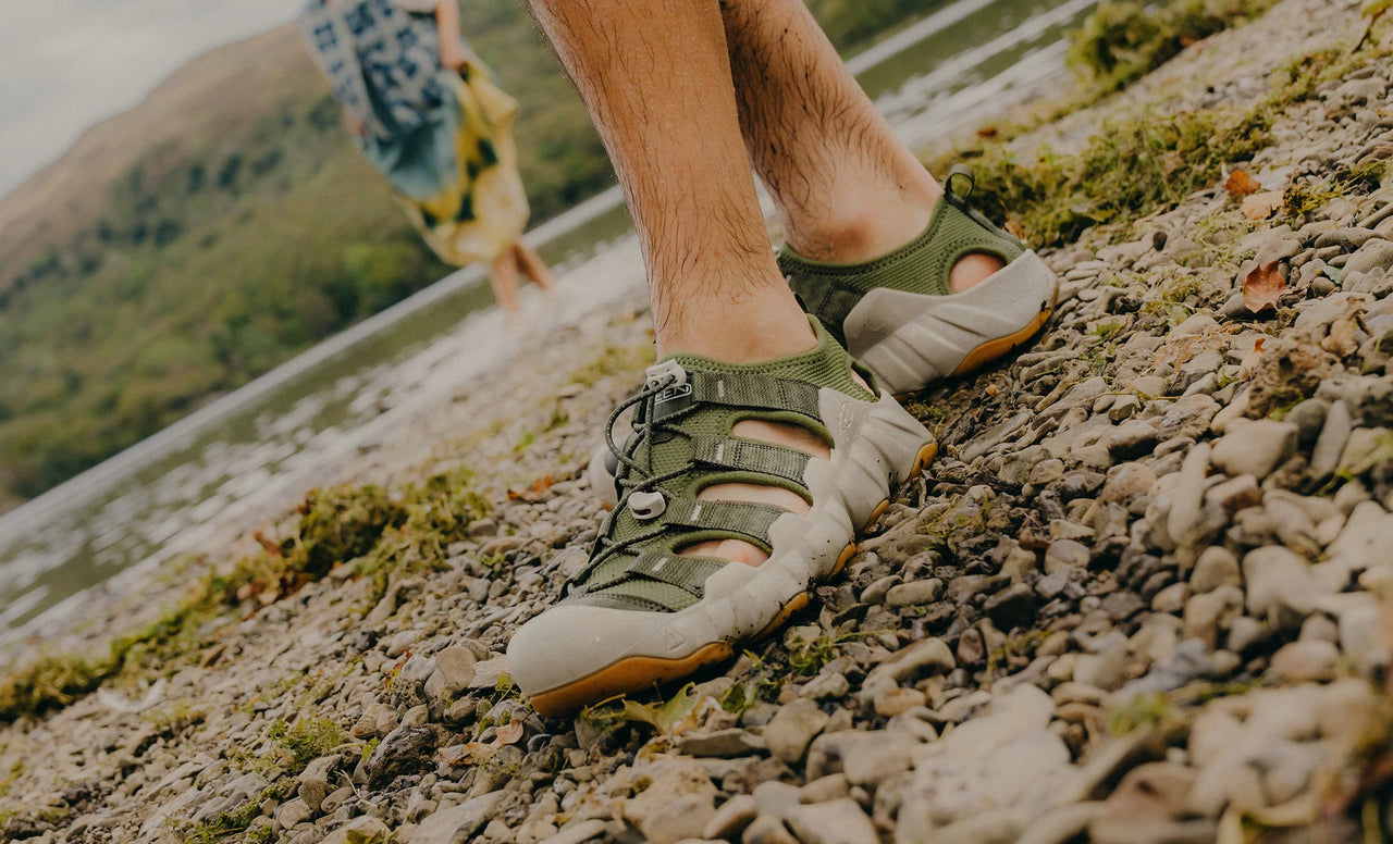 Man wearing green hyperport sandals on a gravel path next to a river