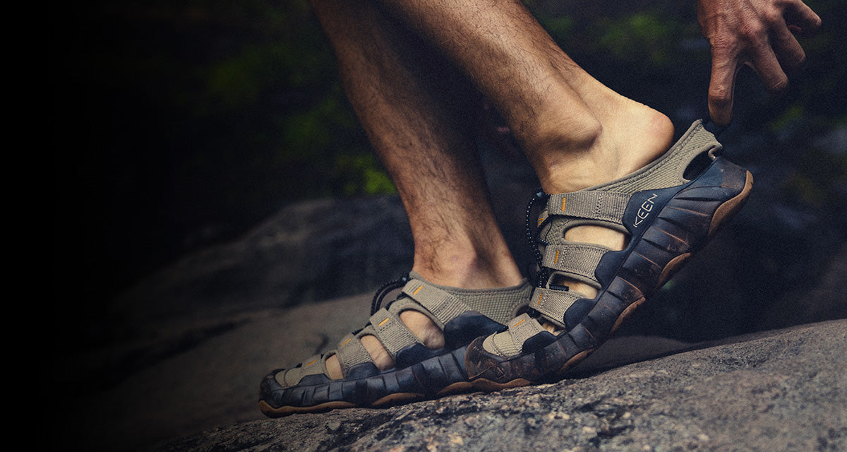 KEEN hiking sandals with adjustable straps and rugged rubber outsoles gripping a rocky surface, highlighting protective toe coverage, cushioned midsoles, and trail‑ready traction in an outdoor setting
