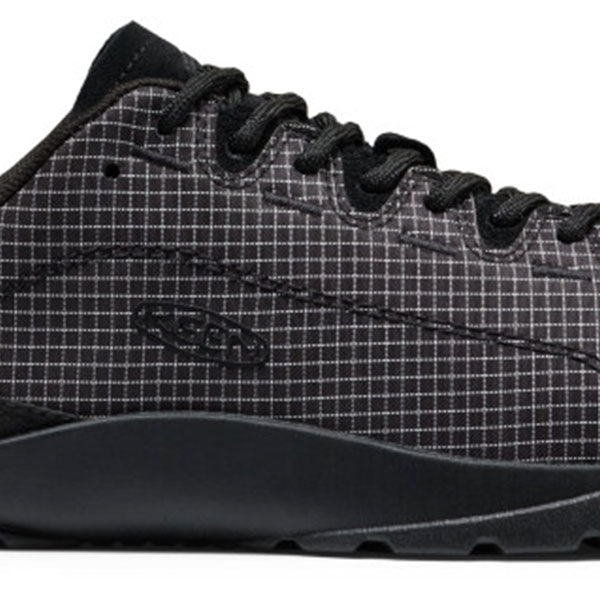 A close-up side view of a black low-top sneaker with a subtle white grid pattern on the upper and a thick black sole, shown against a plain white background.